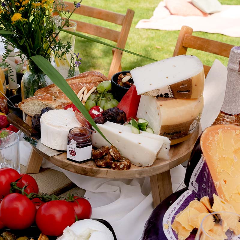 Kaasplank met Chevretta geitenkaas, tomaatjes en druiven buiten op tafel | Kaas & Borrelz