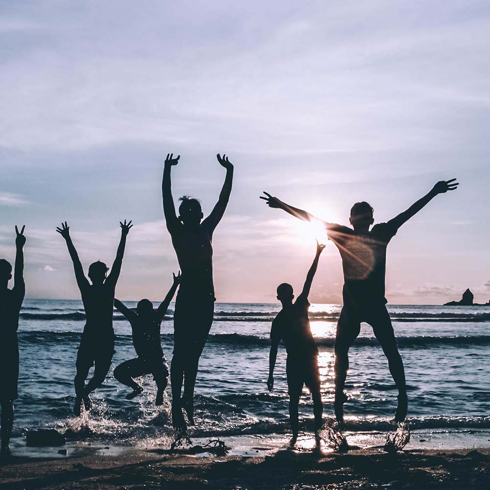 Vrolijke mensen springen bij zonsondergang op het strand, Kaas met Mate | Kaas & Borrelz