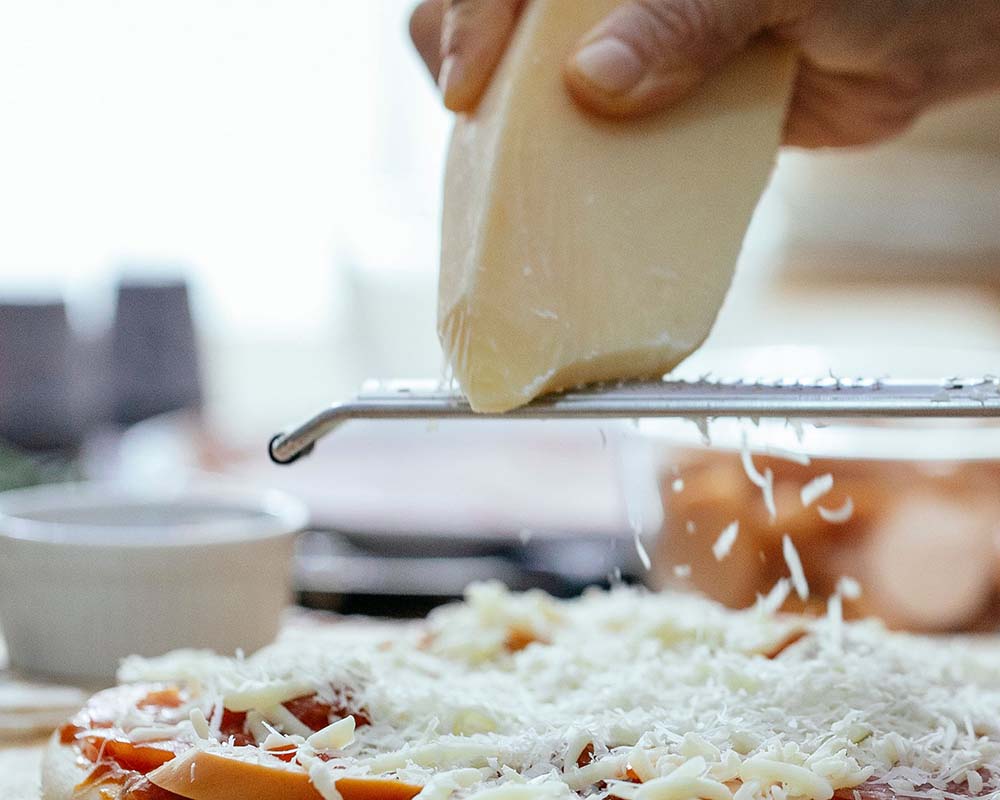 Harde kaas raspen over een pizza | Kaas & Borrelz